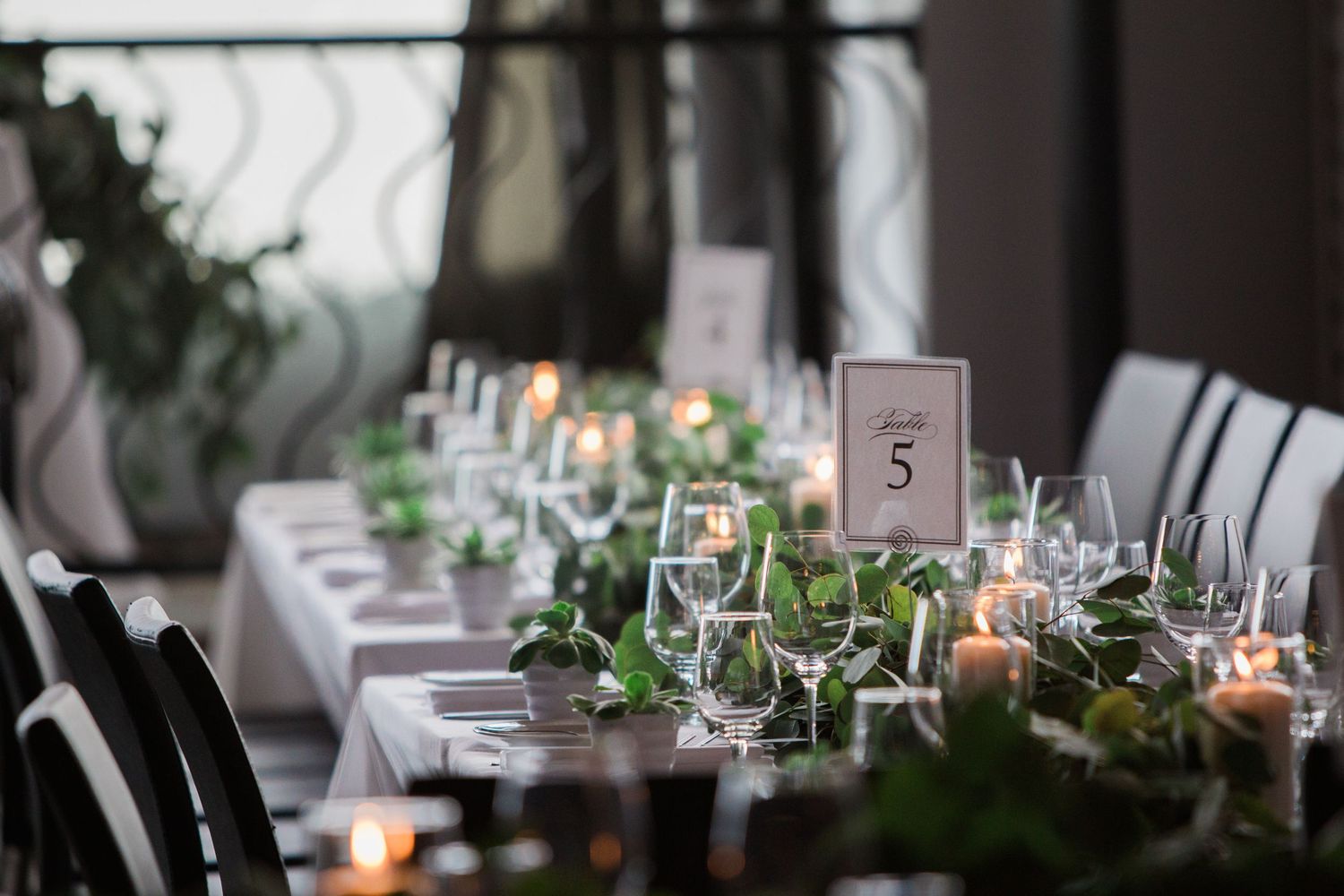 An elegant wedding reception table setting with glowing candles and greenery decorations.