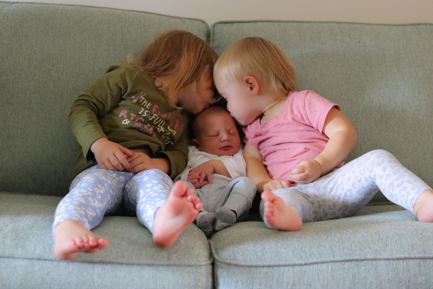 A photo of 3 small kids on the couch, the outter 2 kissing the one in the middle