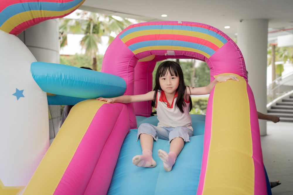 A child enjoying a colorful inflatable bounce house slide with rainbow decorations.