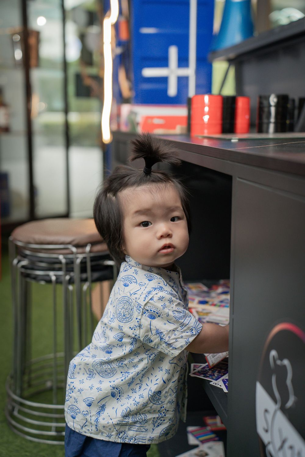A toddler in a floral print shirt explores storage cabinets in a casual setting.