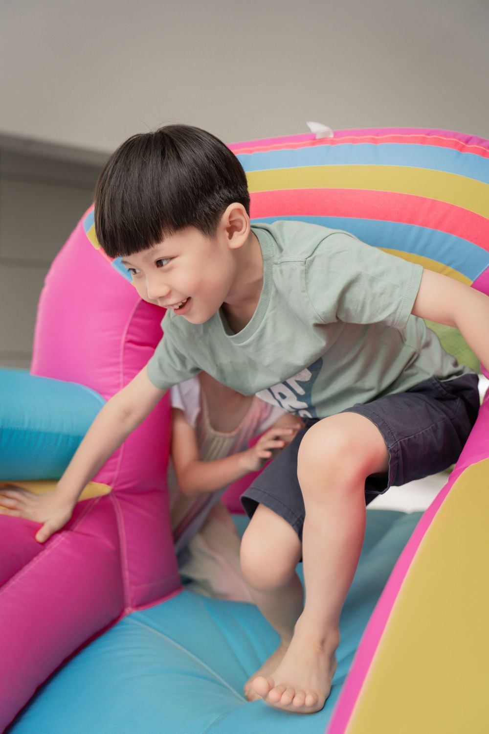 A child playing on a colorful inflatable bounce house with rainbow stripes.