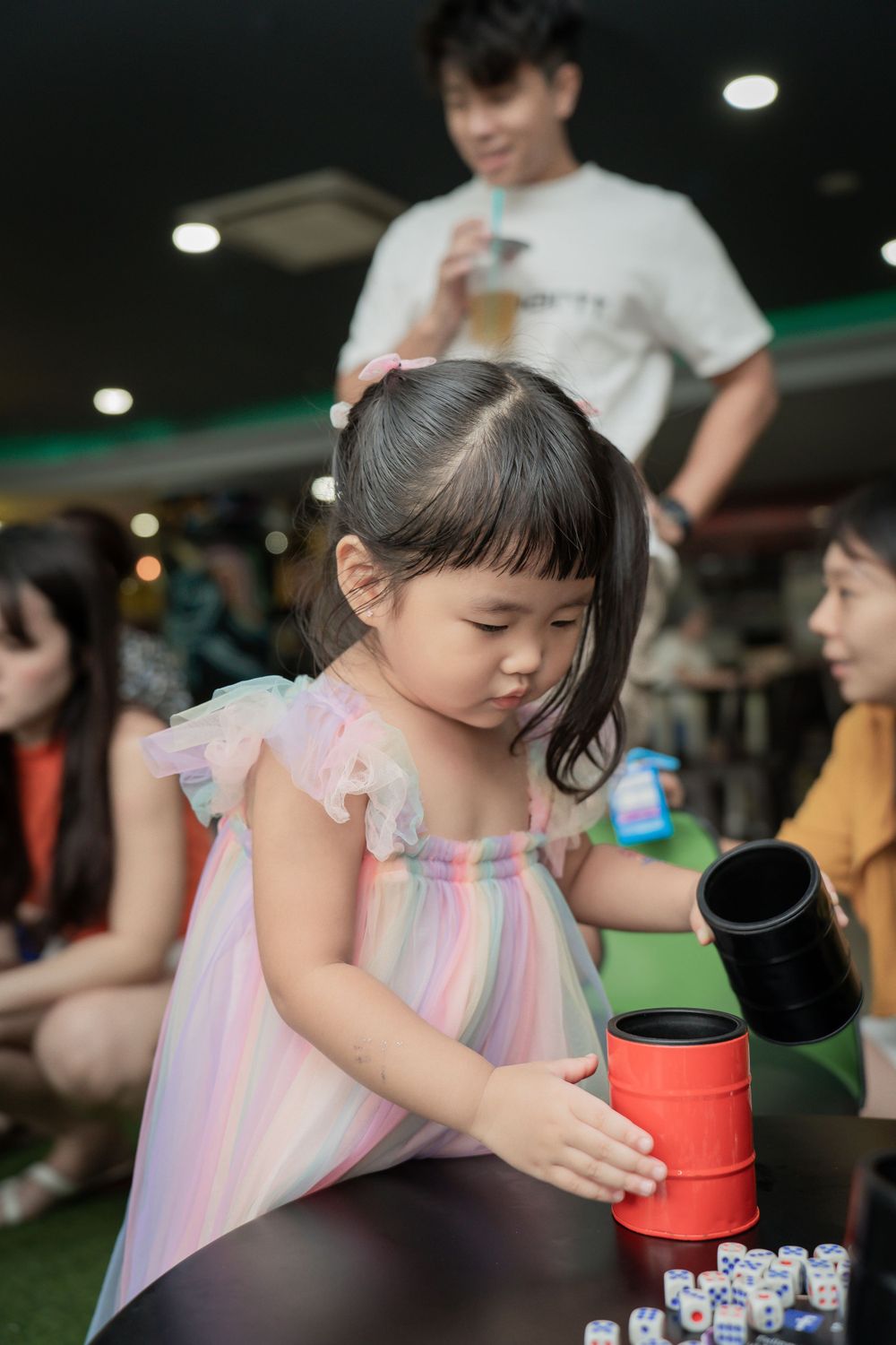 A child in a pink dress participates in a coordination activity game with colored cups at a table.
