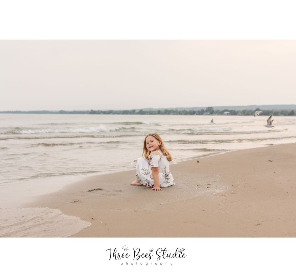 Young girl in white dress playing on beach at sunset.