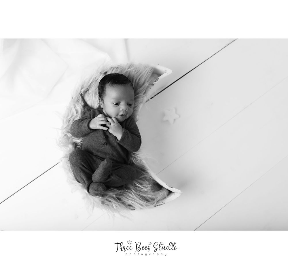 Black and white artistic photo of a baby laying on white floor boards.