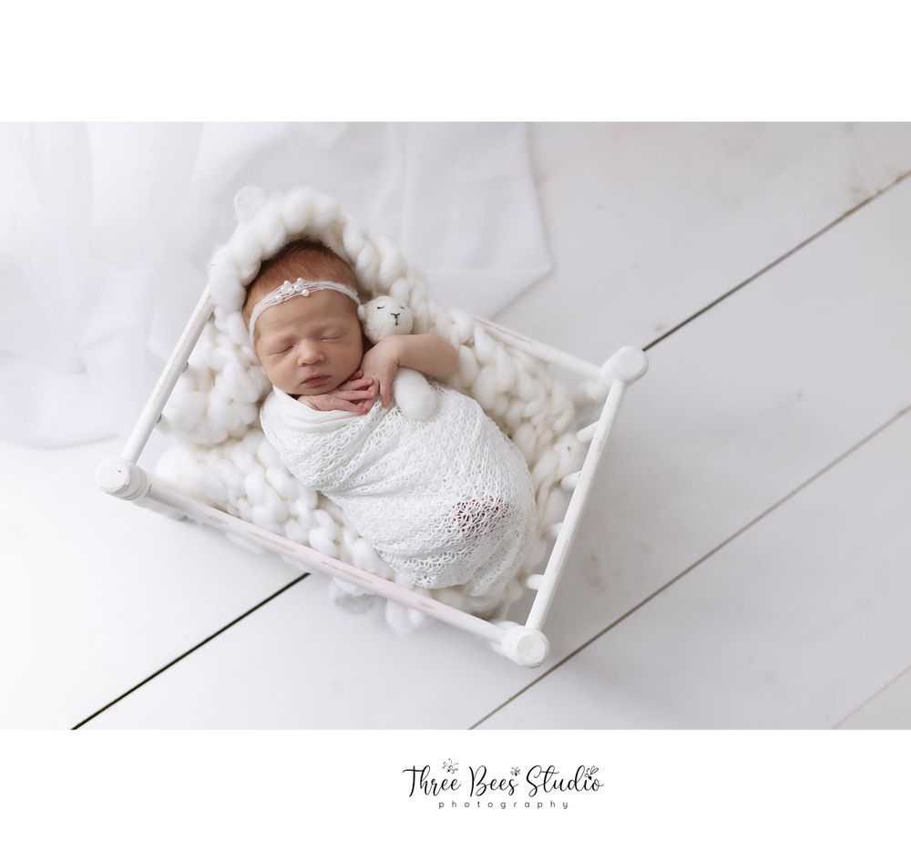 A newborn baby sleeps peacefully in a white basket on wooden floor.