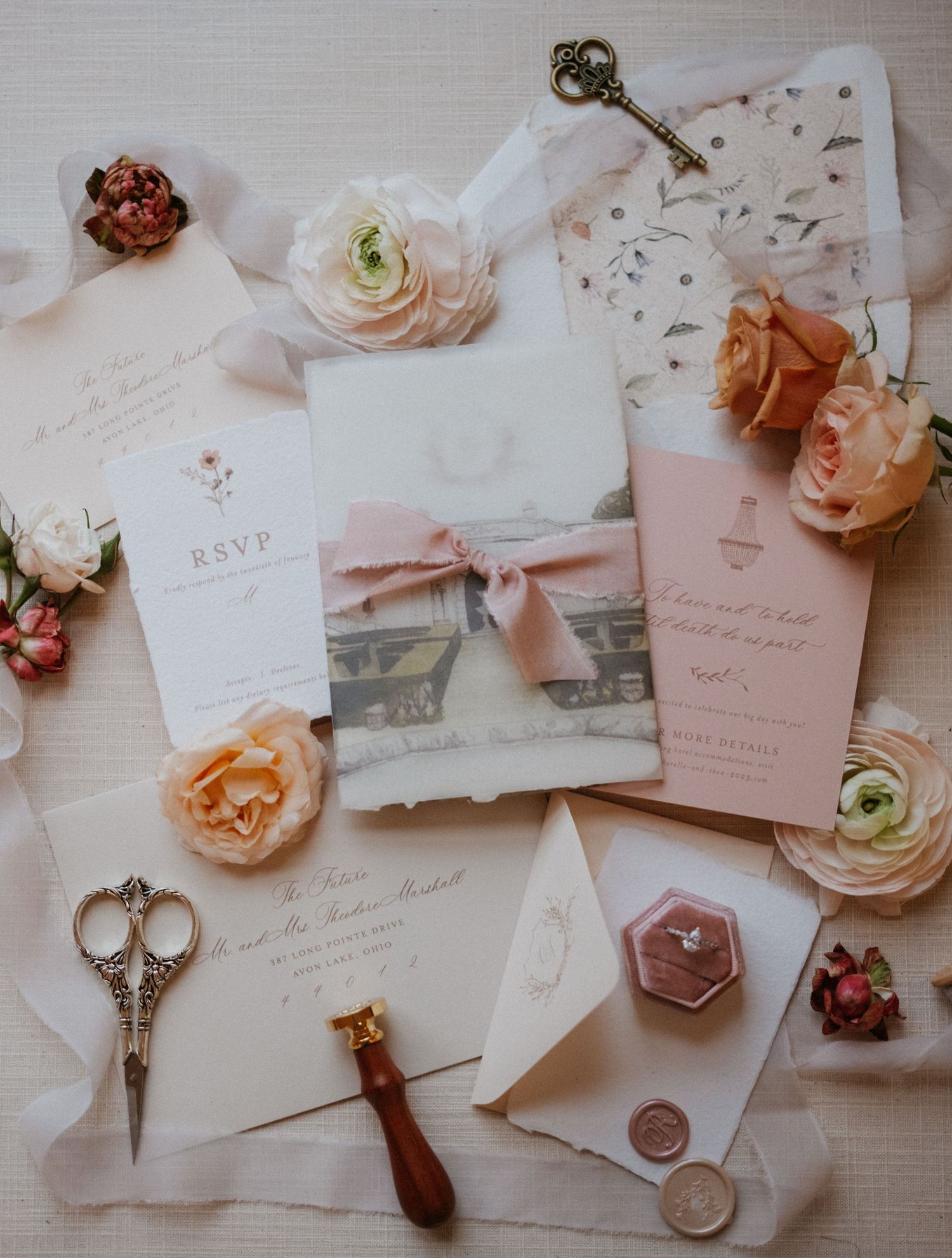 Wedding stationery flatlay with vintage scissors, wax seals, pink ribbon and delicate ranunculus flowers.