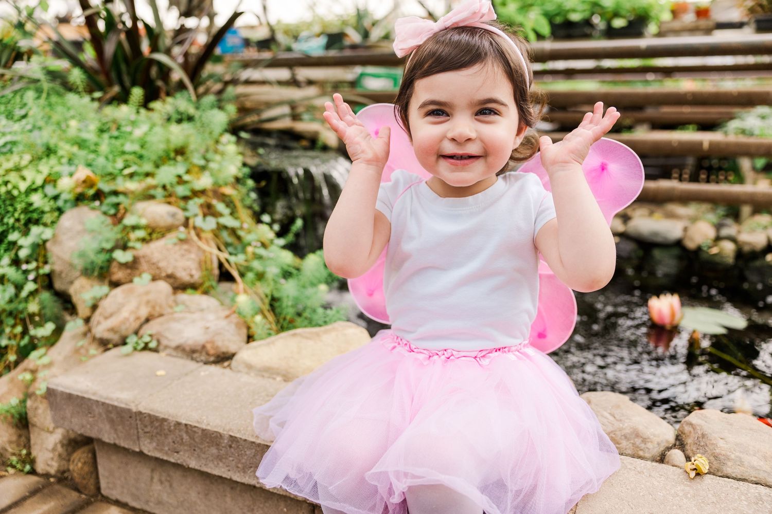 Excited young fairy throws hands up joyfully while playing in garden.