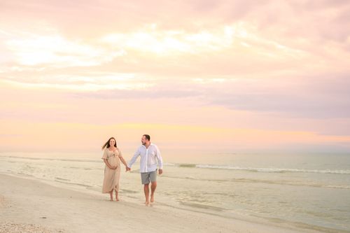 maternity photo of couple walking at beach sunset