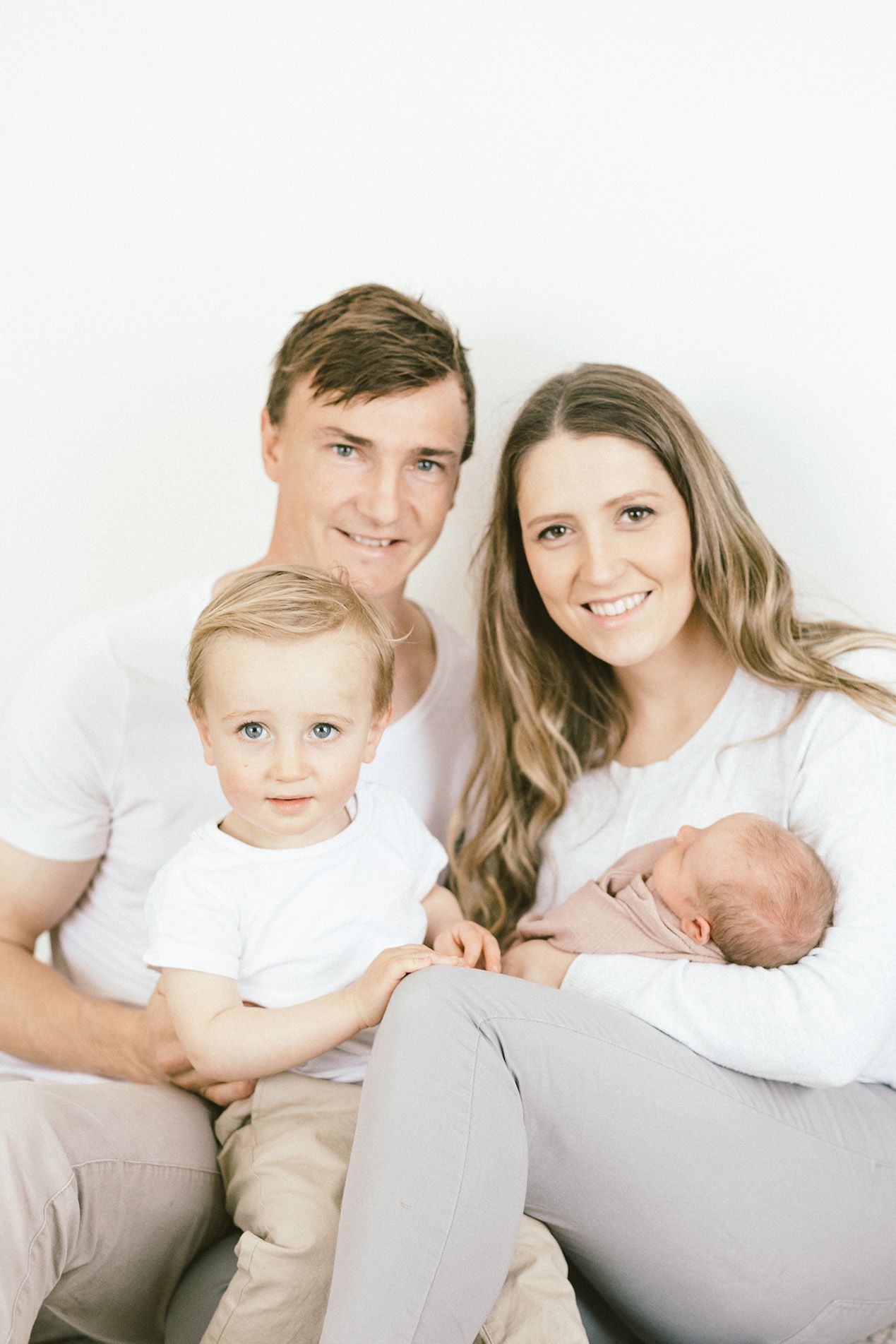 Family portrait series with newborn baby and toddler sibling on white background.