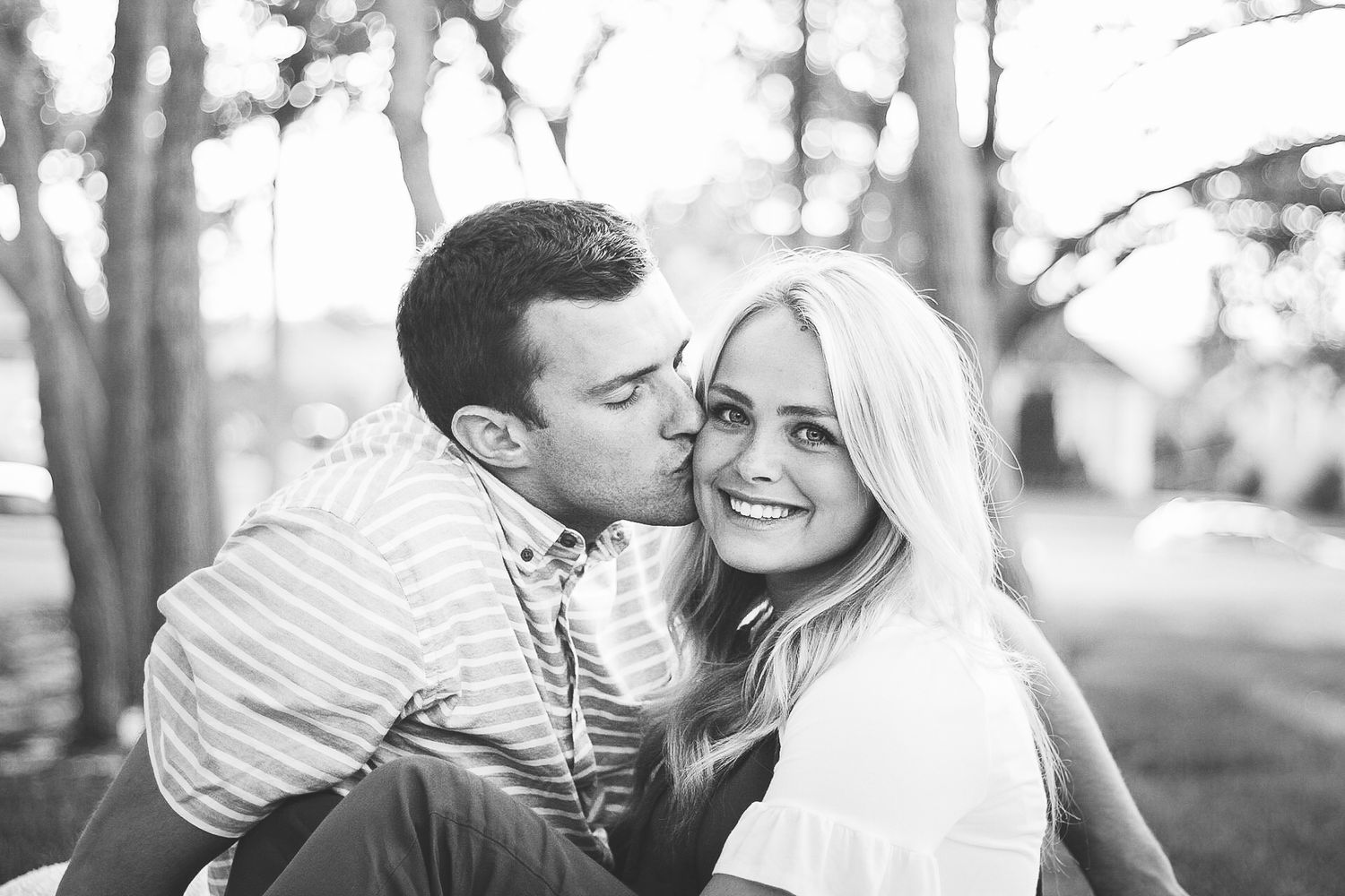 young couple in love sitting on the grass with man kissing woman's cheek and smiling
