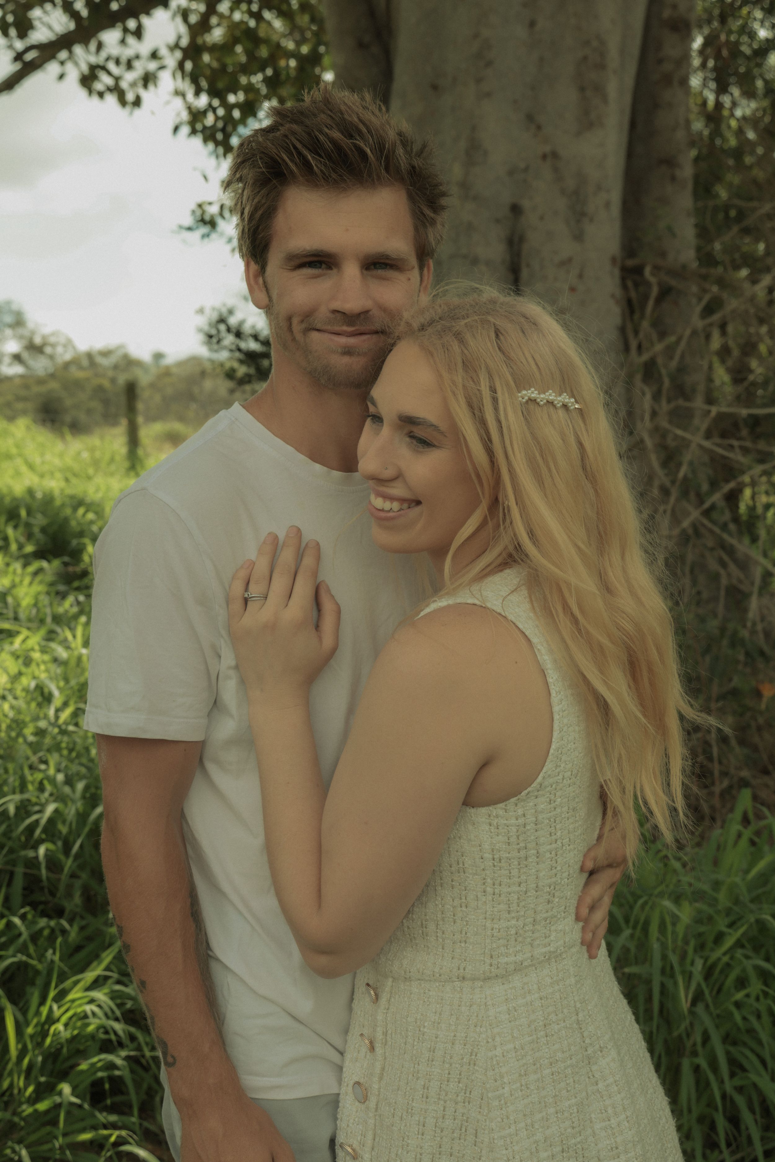 A tender embrace between a couple standing together against a lush green background. Bridget Spark with husband Joshua Spark.