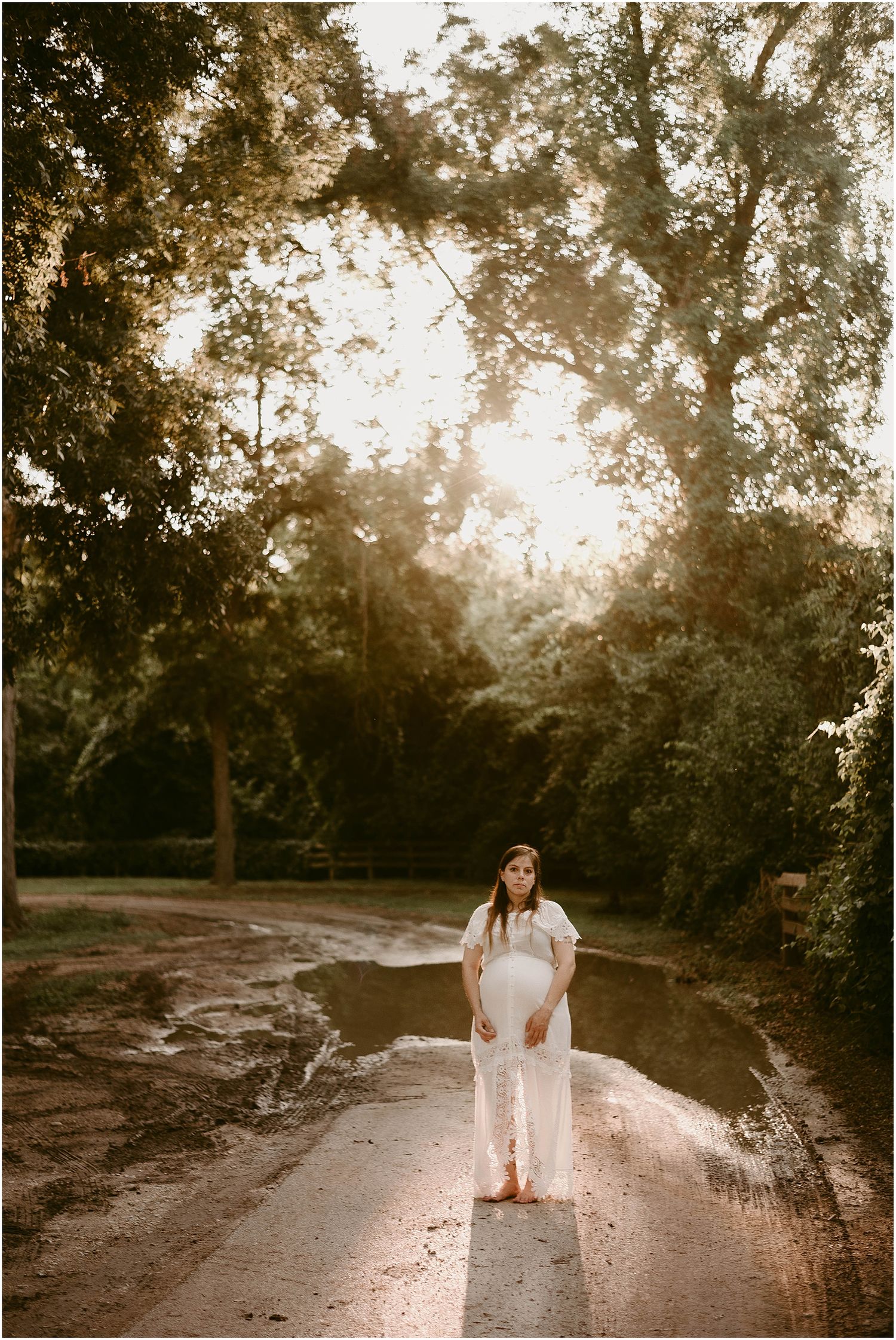 Sunset maternity photo on dirt path with dramatic backlit trees.