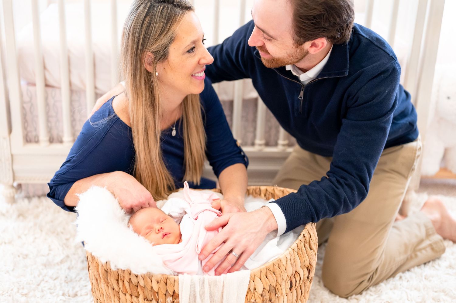 photograph of a couple looking at each other holding their newborn baby girl in a basket during a lifestyle photo