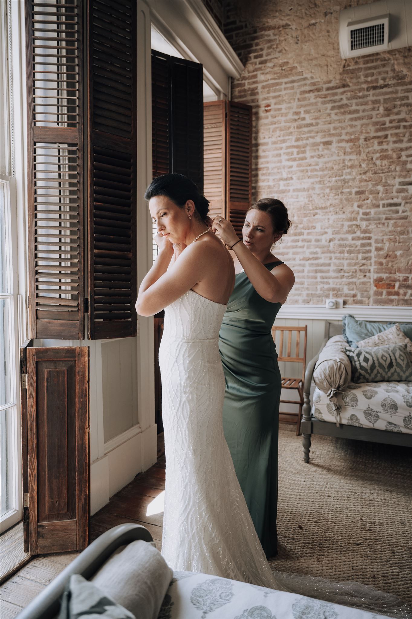 Wedding dress fitting in vintage room with exposed brick walls and wooden shutters.