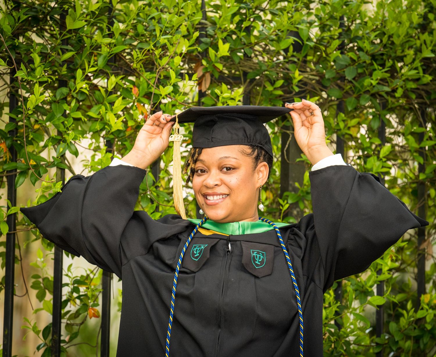 Graduate in cap and gown posing joyfully outdoors with greenery background.
