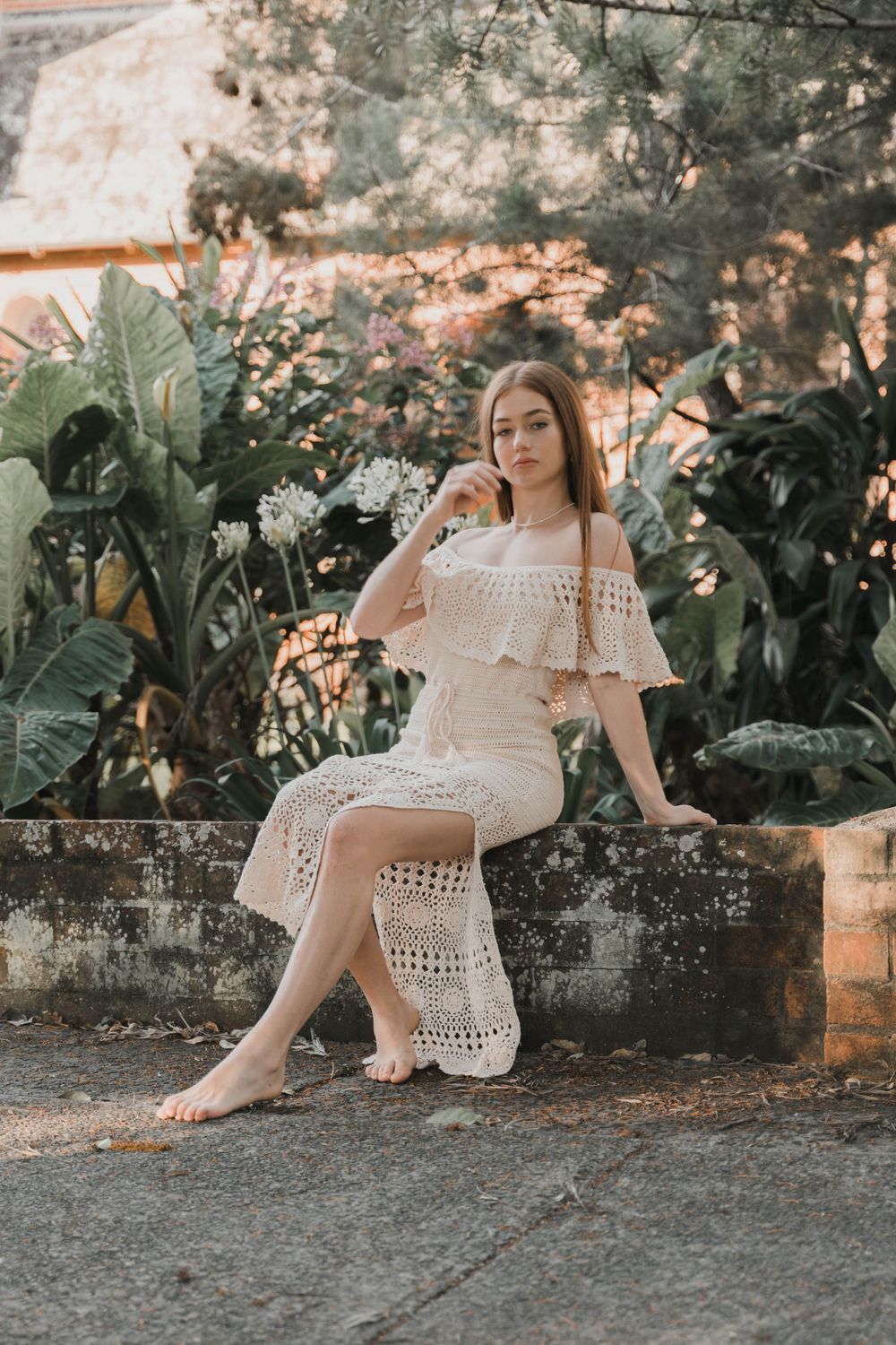 White crochet dress with ruffles photographed against lush tropical garden background.