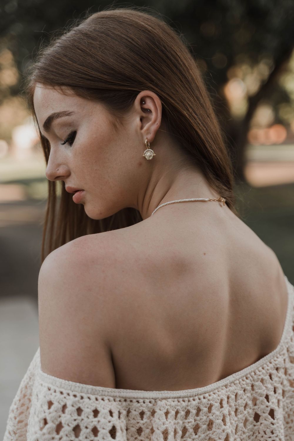 An elegant off-shoulder lace dress shown from behind with delicate earrings and long straight hair.