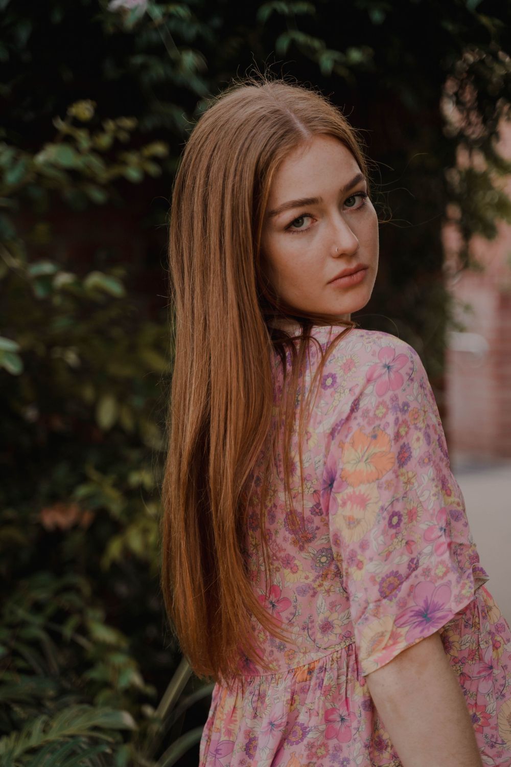 A romantic pink floral dress photographed against lush garden foliage.