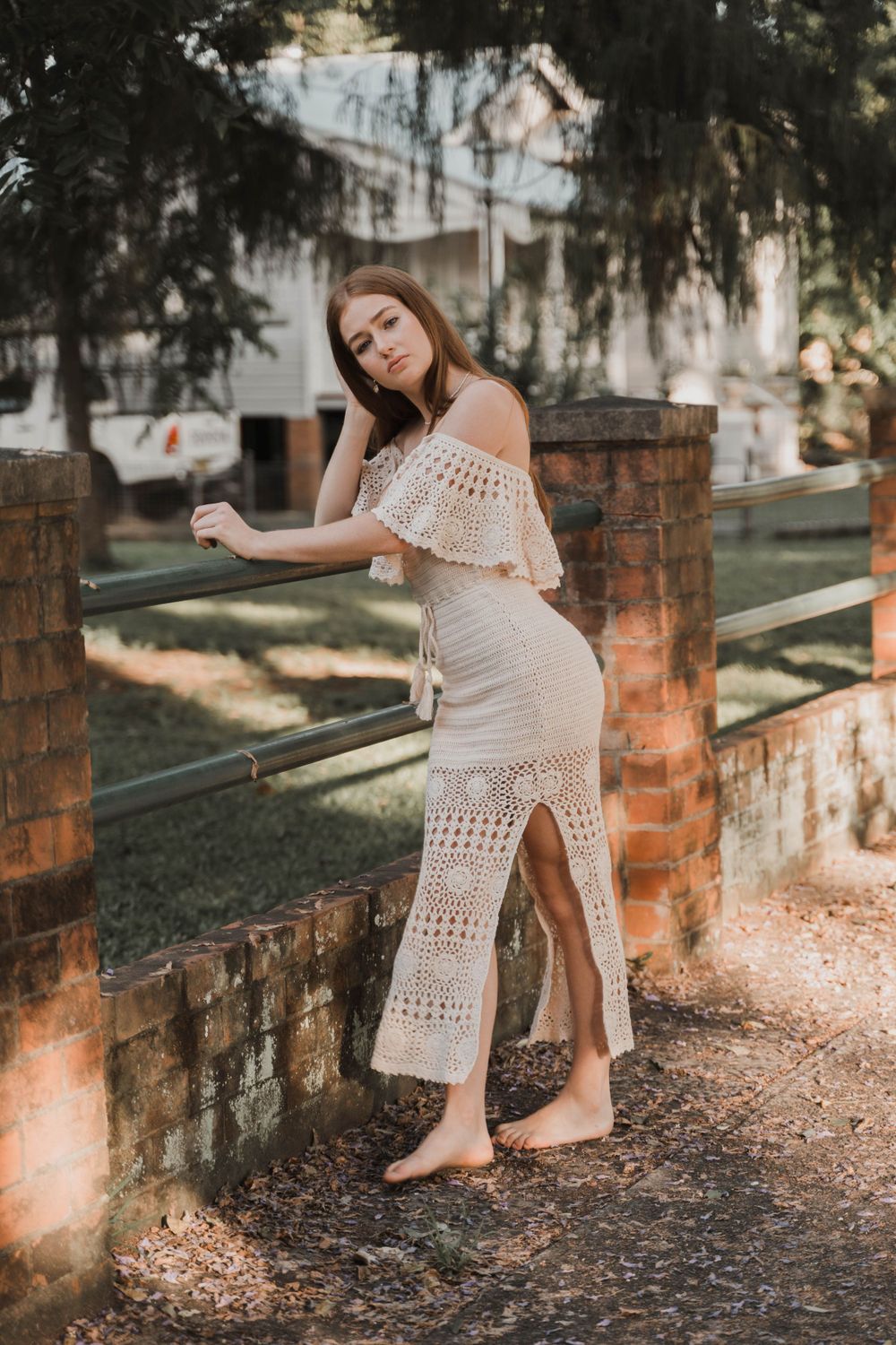 Bohemian style white crochet maxi dress with side slit photographed against brick pillars.