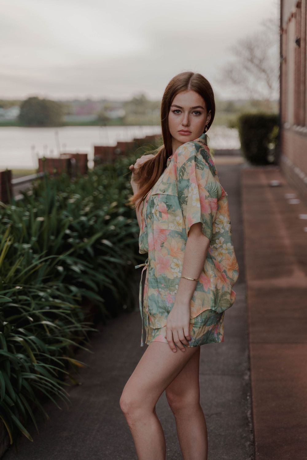 A pastel floral print outfit styled against a moody waterfront backdrop with greenery.