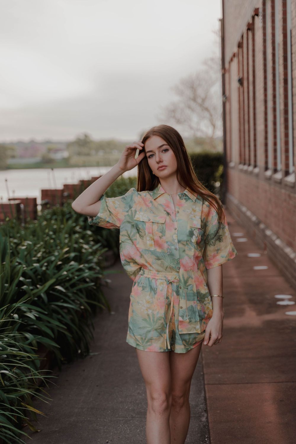 A floral print romper worn on a waterfront walkway with lush garden landscaping.