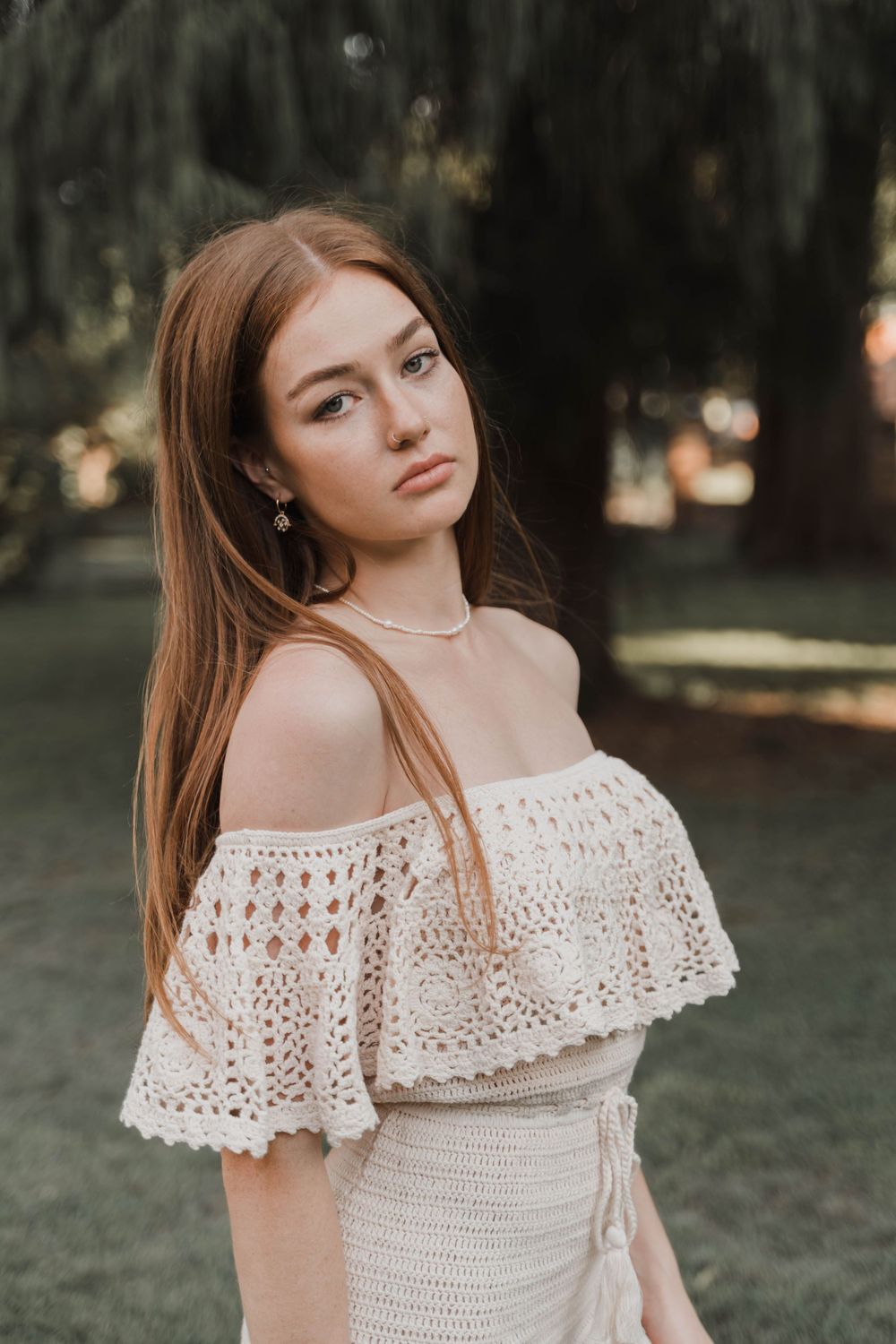 Off-shoulder cream crochet dress with delicate jewelry photographed in outdoor garden setting.