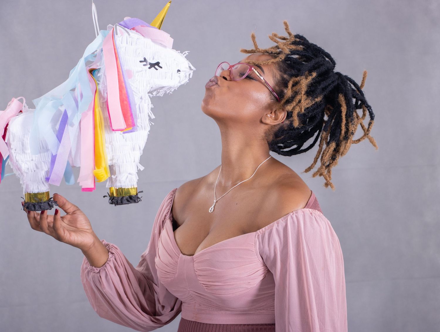 Playful studio portrait with unicorn piñata against grey background.