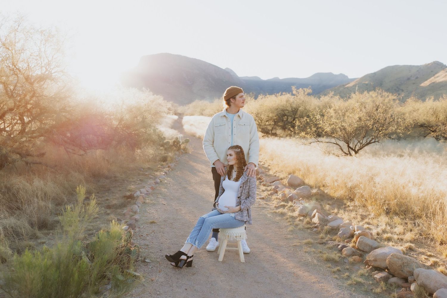 Golden hour sunlight illuminates dirt path with mountains and desert brush.