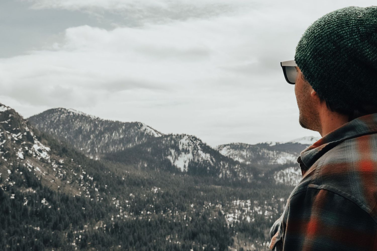 Person wearing plaid and beanie looking out at snow-capped mountain landscape.