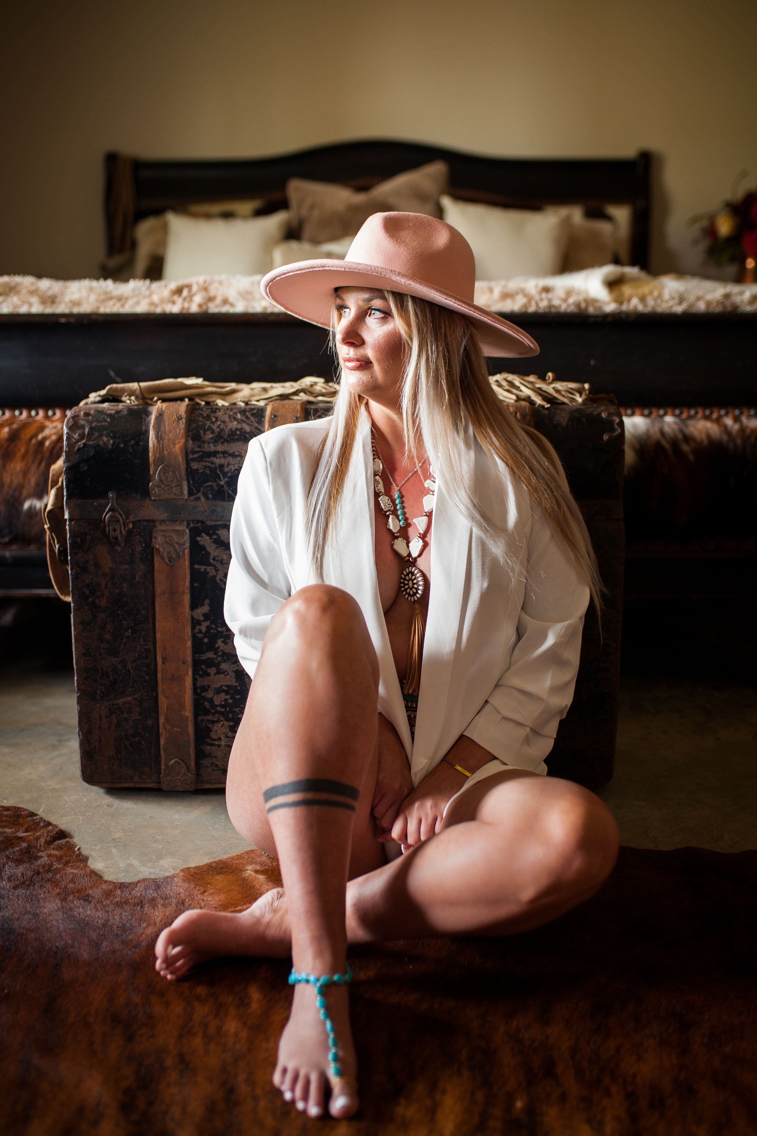 Woman in white shirt and pink hat poses on floor near vintage trunk.
