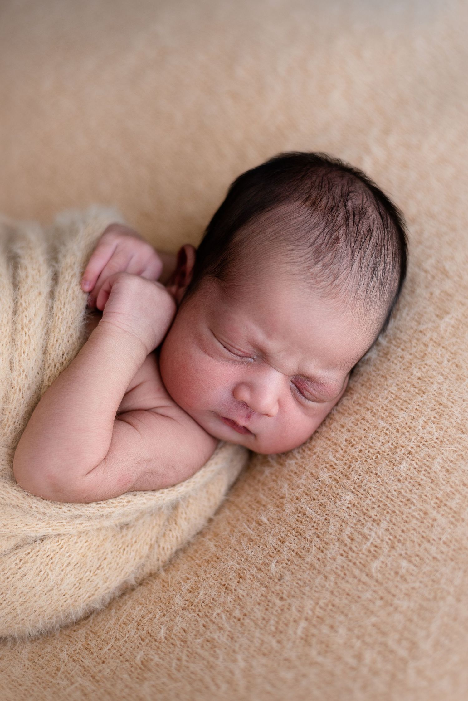 Peaceful sleeping newborn wrapped in soft beige blanket on textured surface.