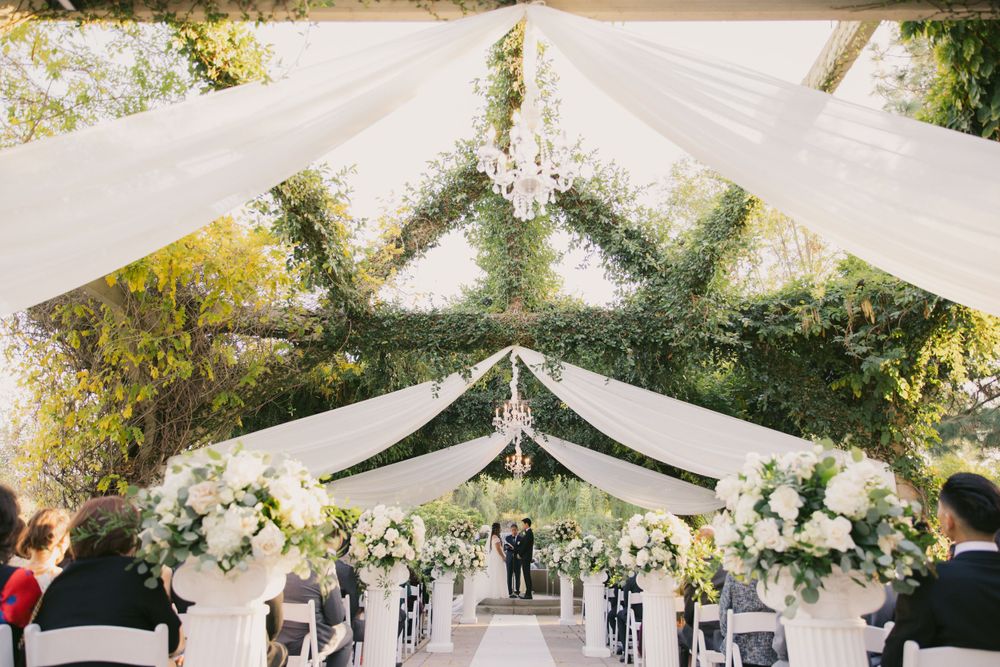 Elegant white wedding tent decorated with floral arrangements and draped fabric.