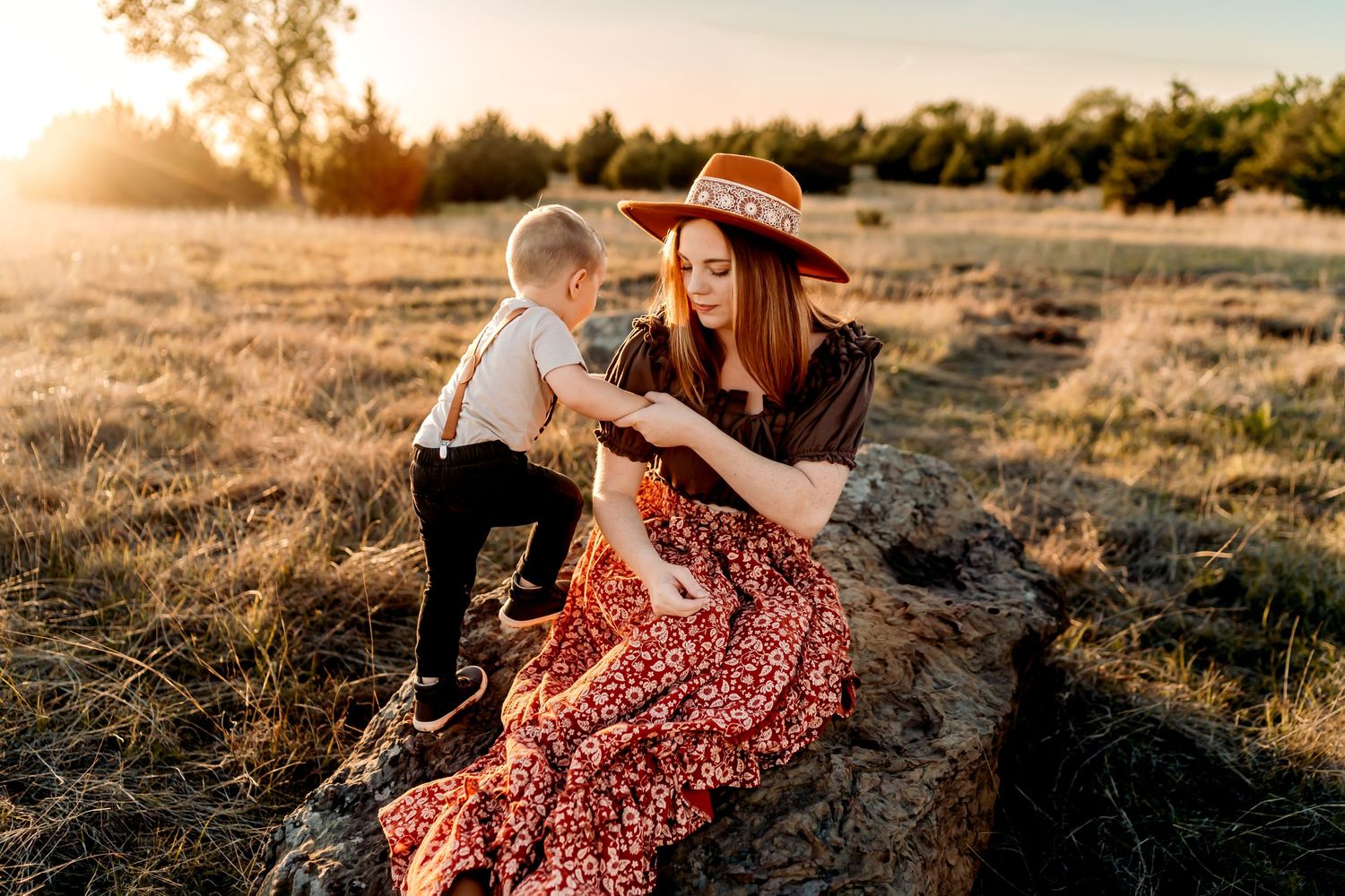 Sunset field portrait with toddler and woman in floral dress sitting on rocky outcrop.