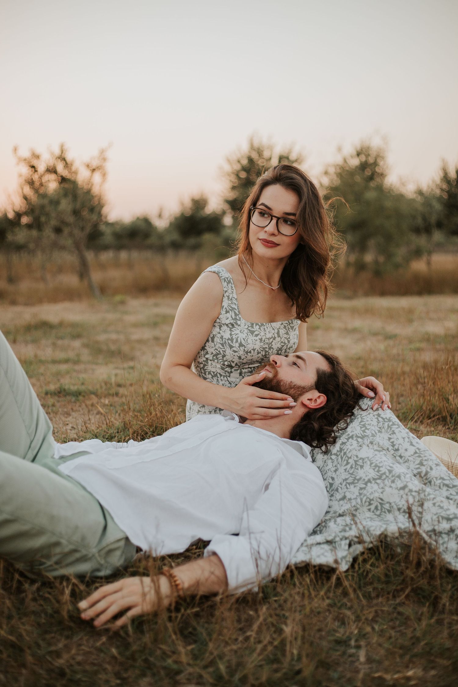 A romantic couple lounges in a rustic field during sunset.