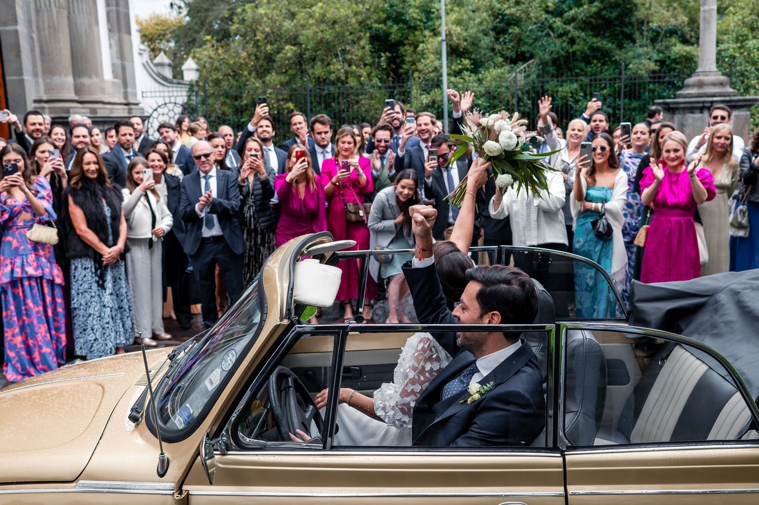 A large crowd gathers outside for a celebratory event with colorful formal attire.