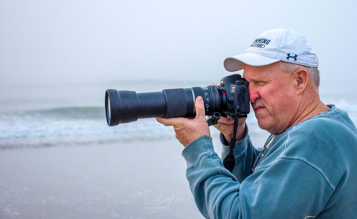 Photographer with a telephoto lens capturing photos at a misty beach.