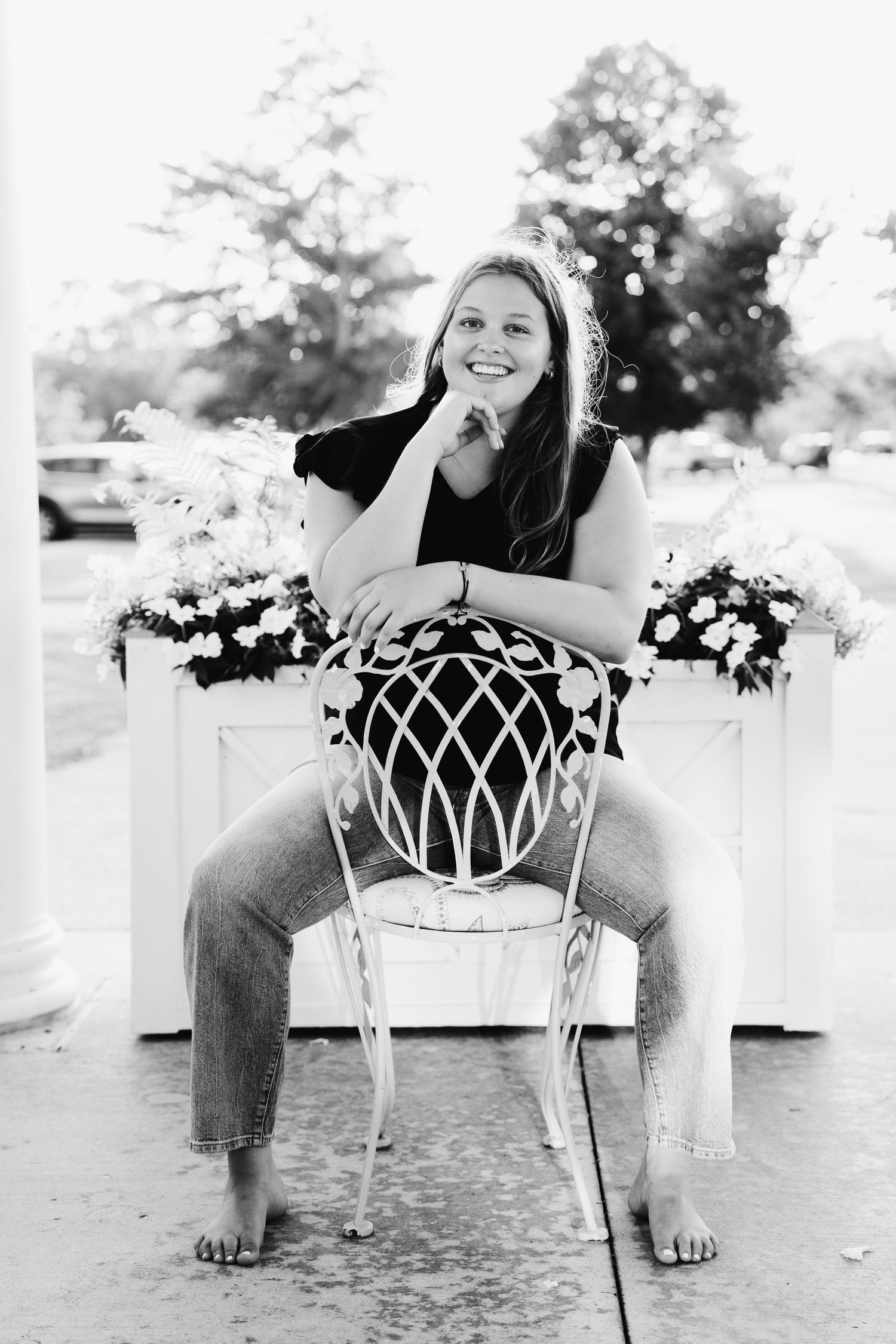 Black and white portrait of girl smiling, seated backward on chair with chin in hand, shot by Milwaukee senior photographer Rachel Dickman.