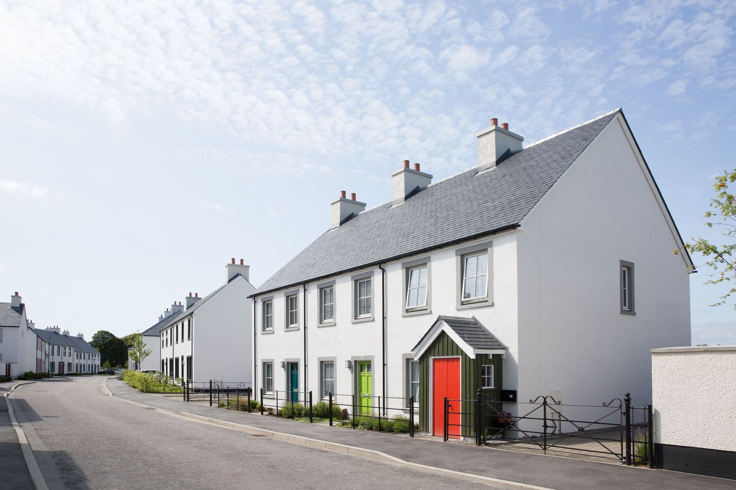 Row of modern white townhouses with red door along quiet street in daylight.