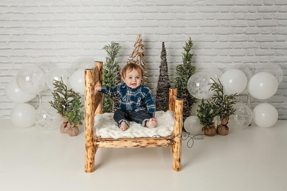 Rustic wooden bench with decorative trees and white balloons creating winter scene against brick backdrop.