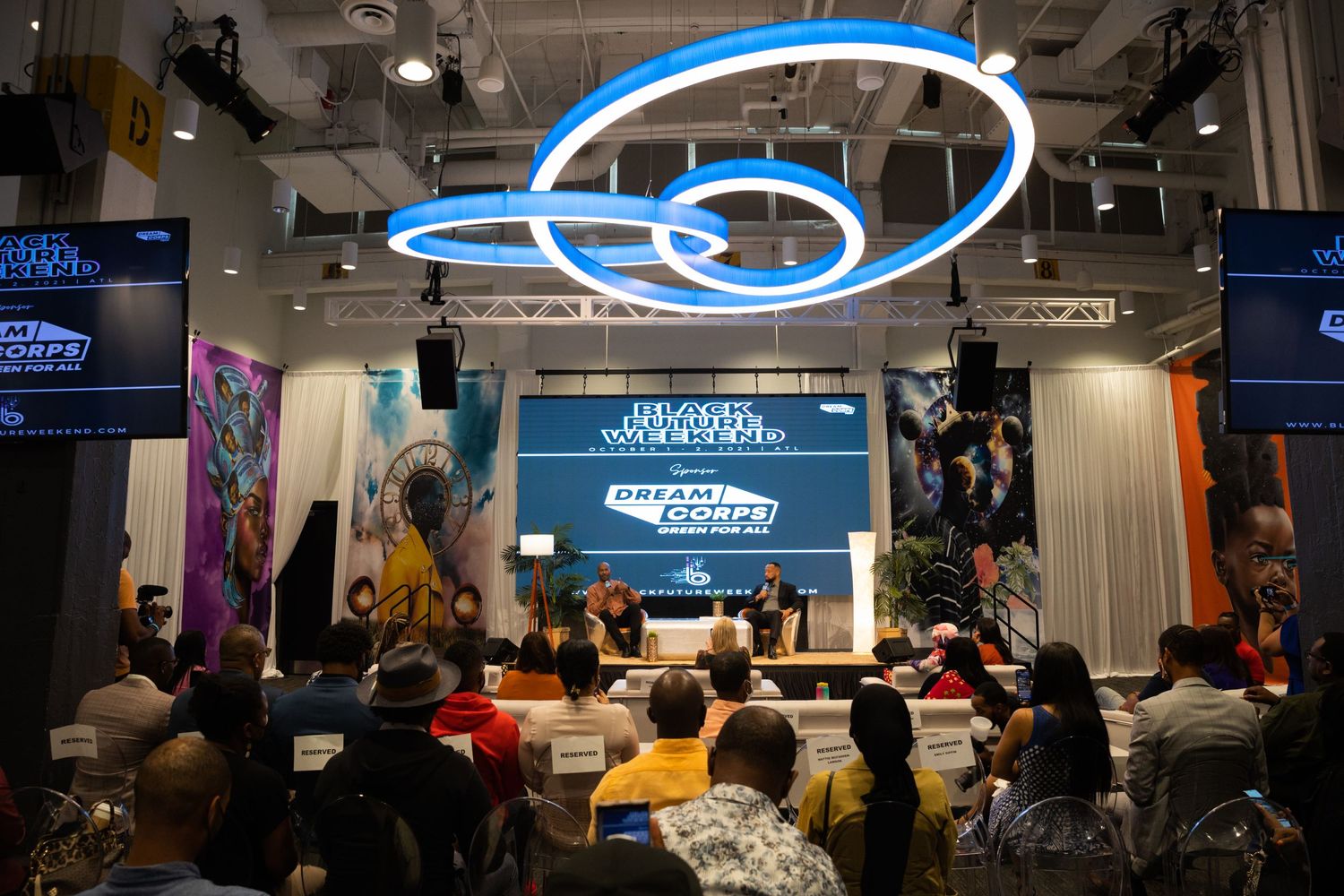 An audience watches a panel discussion at a Black Women in Tech Dream Corps event under neon lights.