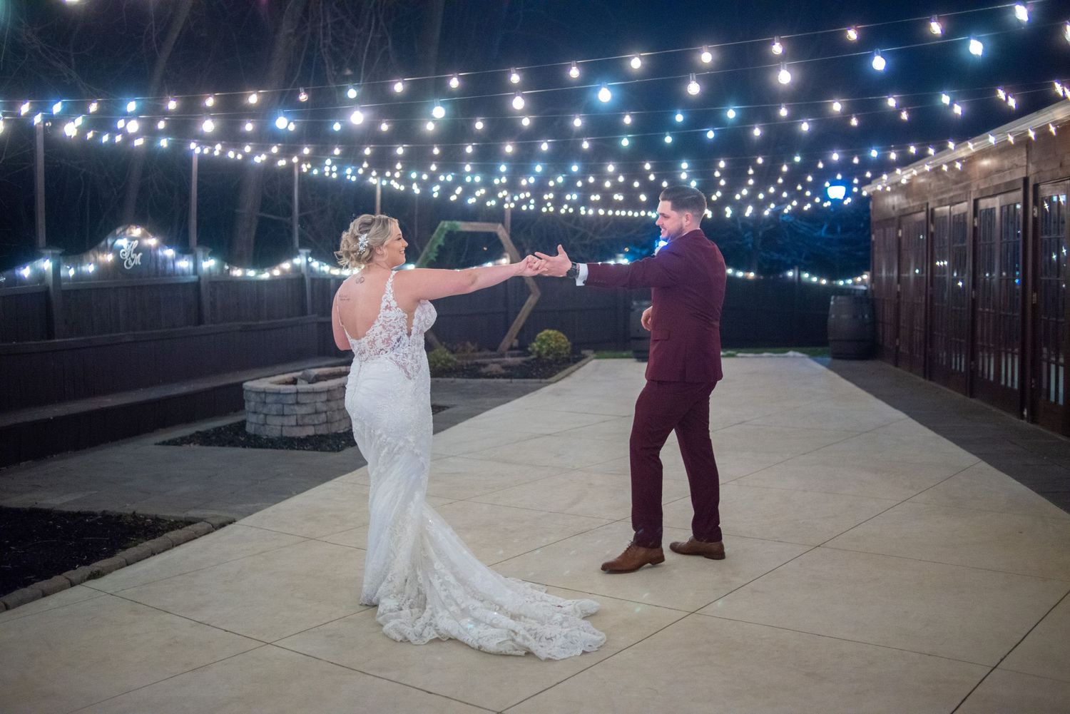 Bride and groom dancing under string lights at outdoor nighttime reception.