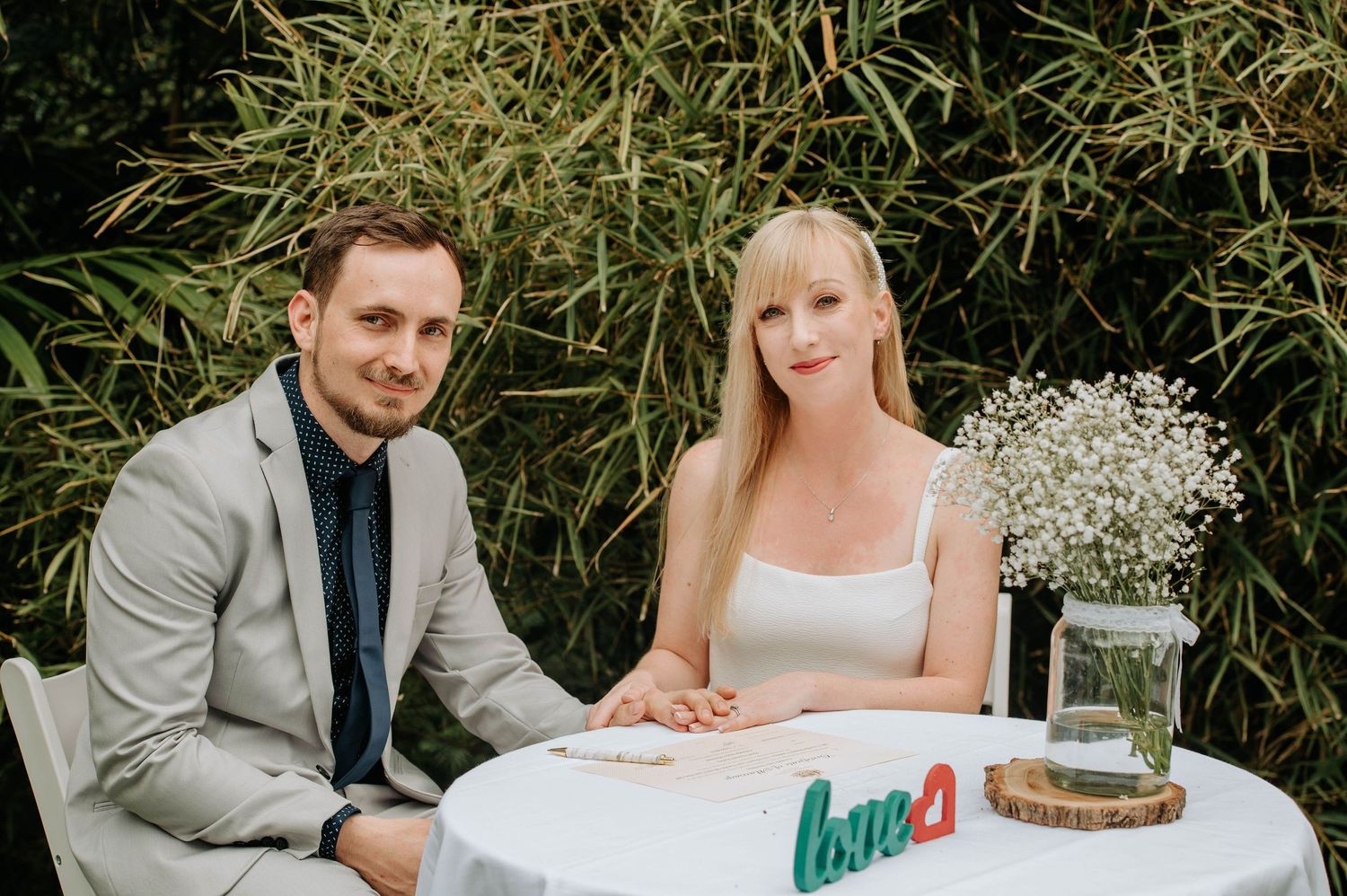 Couple seated at white table with baby's breath centerpiece during garden reception.
