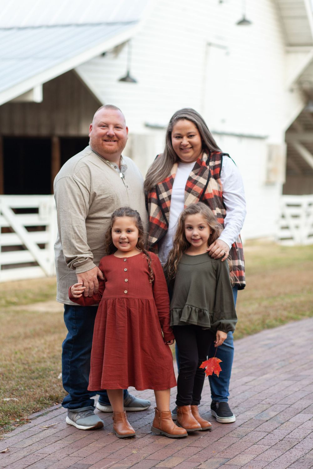 A family stands together on a brick path in front of a white barn on a fall day.