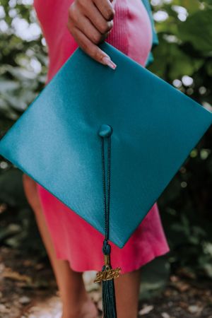 Close-up of teal graduation cap being held against pink dress in natural lighting.
