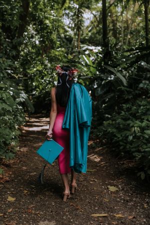 Two people carrying graduation attire walk along a wooded path.