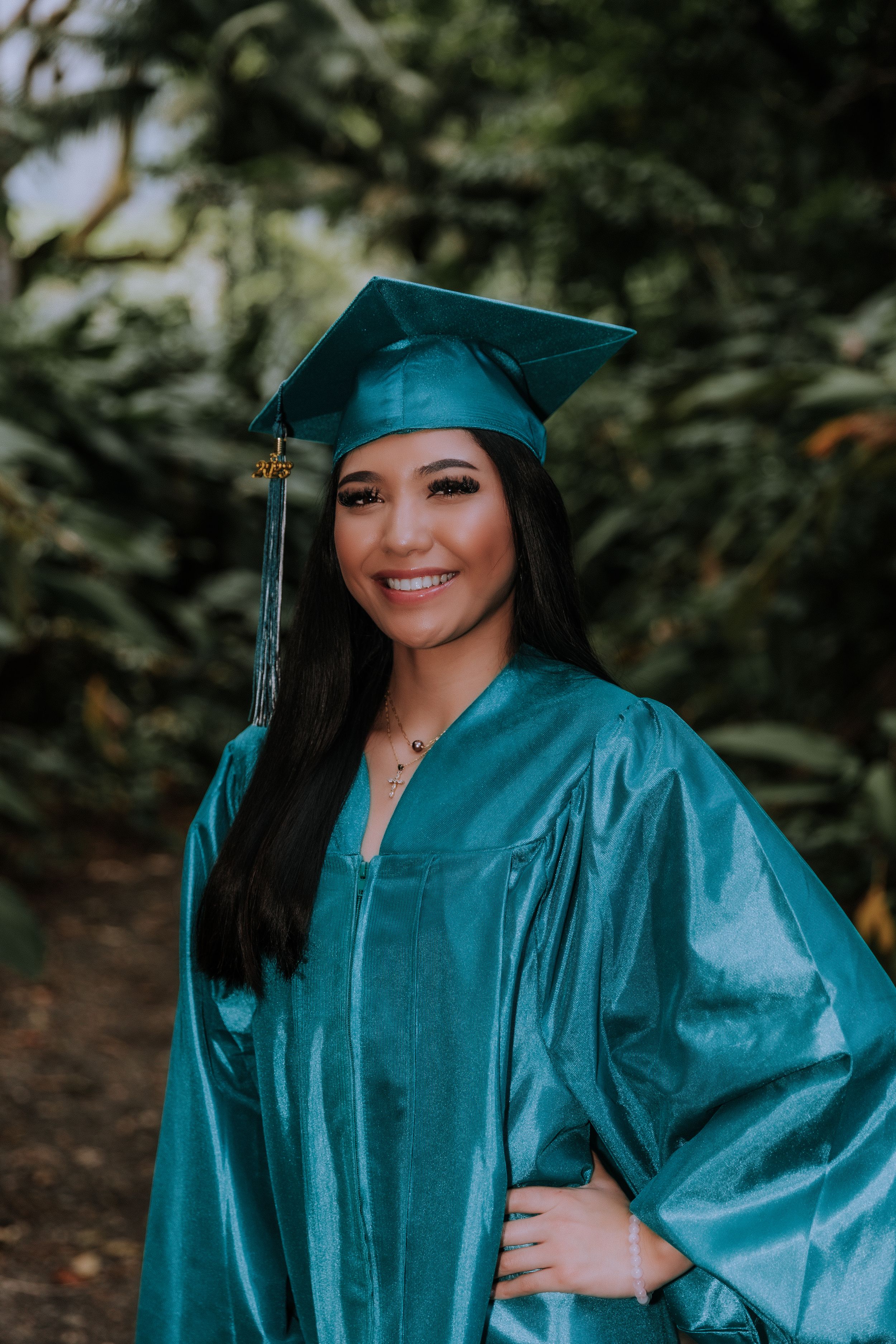 Teal graduation cap and gown photos with natural garden backdrop.