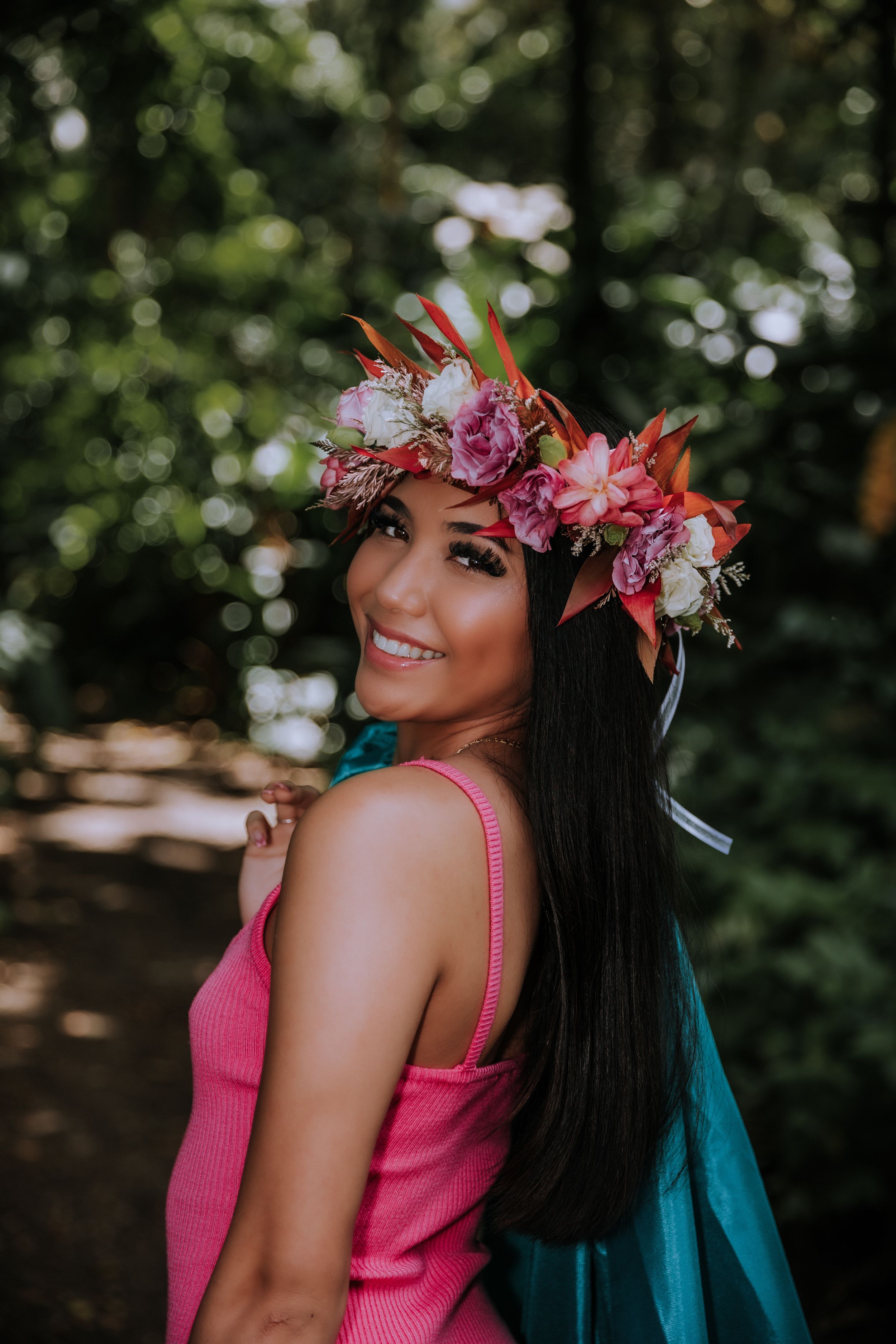 Floral crown and pink dress create a dreamy graduation portrait in a wooded setting.