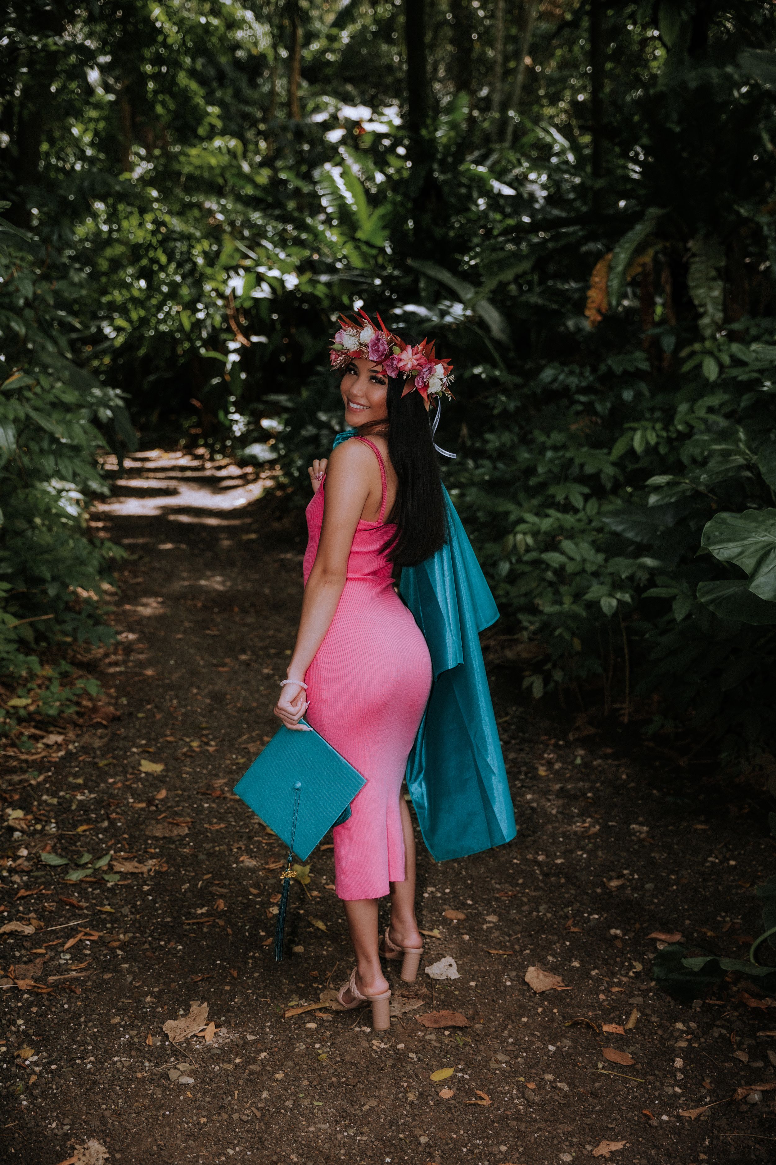 A graduation photoshoot in a lush garden setting featuring pink dress and teal graduation gown.