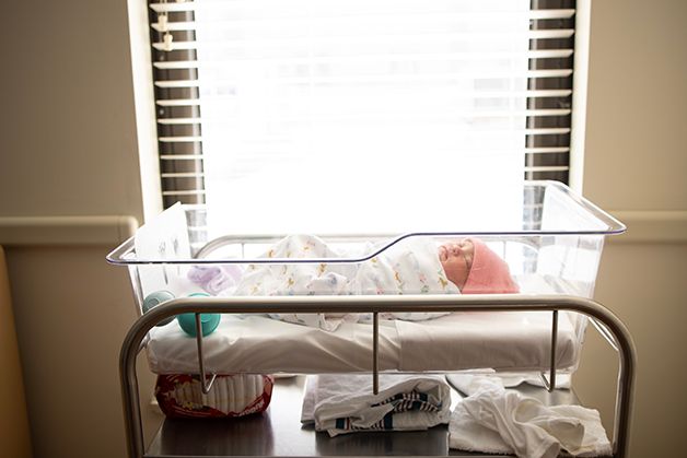 Newborn baby girl in hospital bassinet.  Light from the window is cascading over the bassinet.