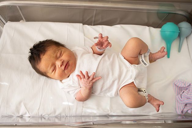 Newborn baby girl in white onesie laying in the hospital bassinet.